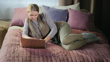 a middle-aged woman uses a laptop on her bed 1