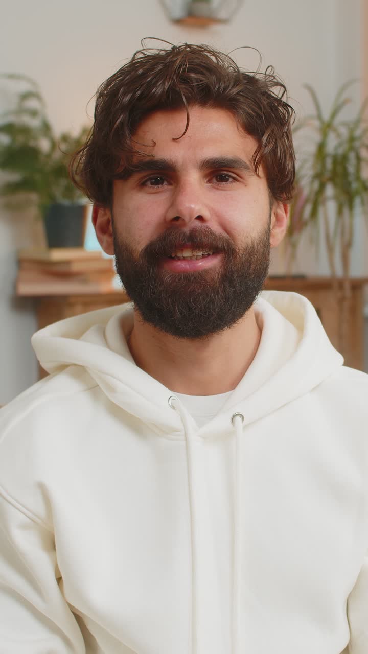 Portrait of happy young indian man looking at camera and smiling while sitting on sofa at home
