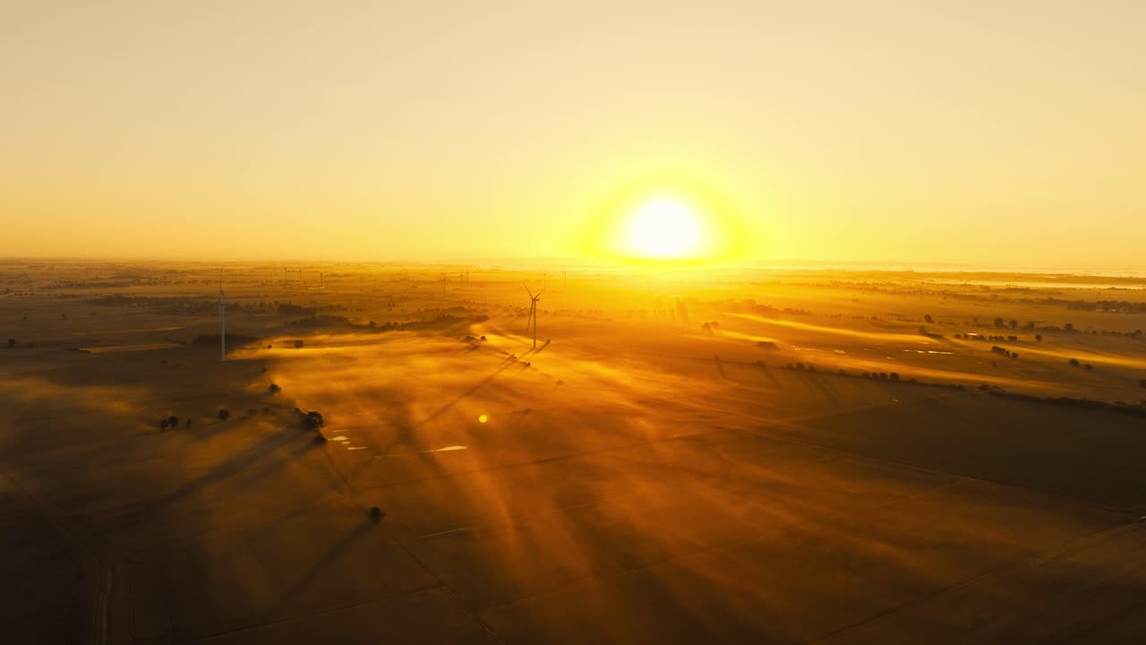 Sun dips below horizon as golden mist glows over wind turbines and fields