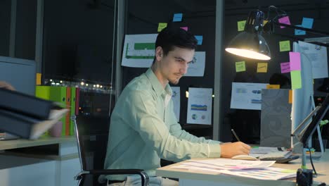 hombre de negocios sobrecargado de trabajo trabajando hasta tarde en la noche en la oficina, su escritorio está cubierto de papeleo, horas extras de trabajo y concepto de plazos