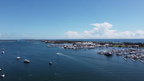 Vista-Aérea-De-Un-Puerto-Y-Una-Bahía-Con-Veleros-Y-Un-Barco-De-Motor-Que-Pasa