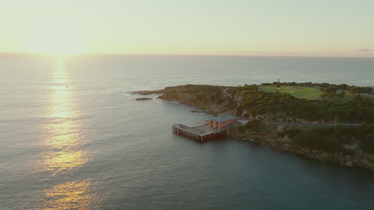 Aerial: Drone descending towards Tathra Wharf as the golden sun rises over the ocean, South Coast NSW, Australia