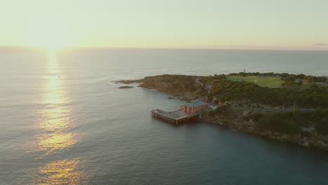 aerial: drone descending towards tathra wharf as the golden sun rises over the ocean, south coast nsw, australia