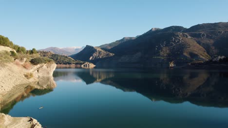 Langsamer-Drohnenflug-über-Das-Wasser-Des-Stausees-Güéjar-Canales-In-Spanien,-Vorbei-Unter-Einer-Brücke,-Die-Zu-Einem-Wasserturm-Führt