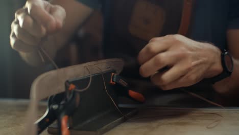 medium shot of artisan's hands stiching a handmade leather belt