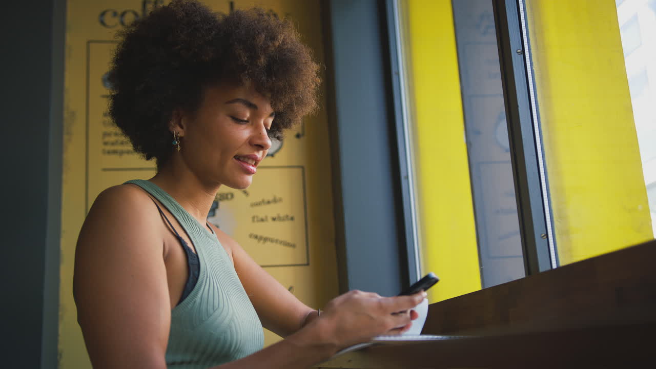 Female Customer In Coffee Shop Window Messaging Using Mobile Phone
