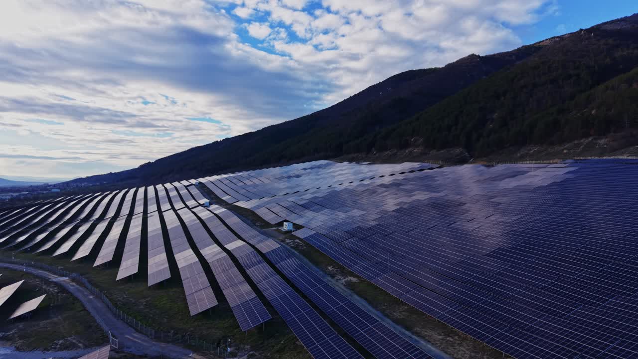 Solpaneler dækker et stort område på en bjergskråning under en skyet himmel