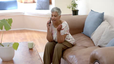 Feliz-Mujer-Birracial-Mayor-Sentada-En-El-Sofá-Y-Hablando-Por-Teléfono-Inteligente-En-Casa,-Cámara-Lenta