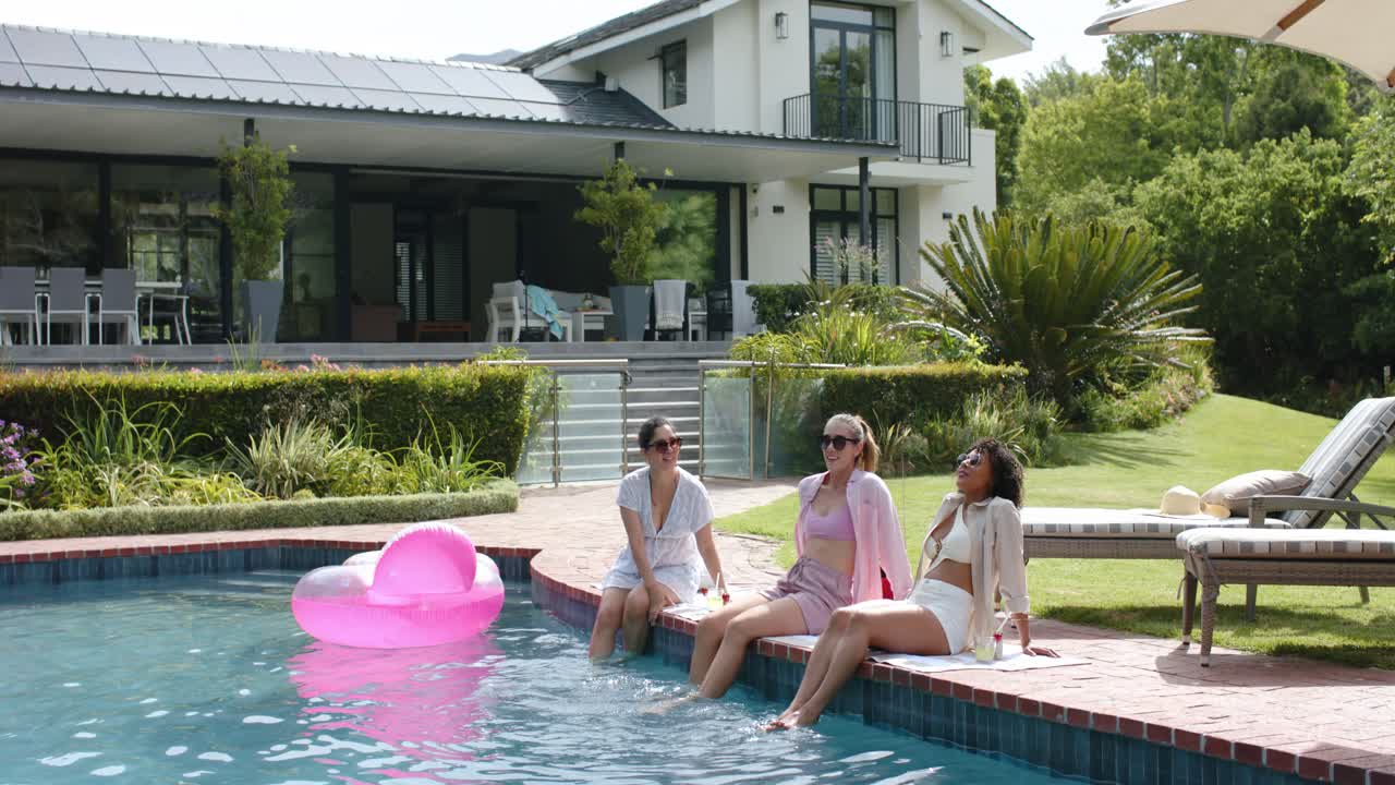 Diverse amiche sedute sul bordo in mattoni della piscina chiacchierano, schizzano l'acqua e danno un'occhiata al galleggiante rosa.