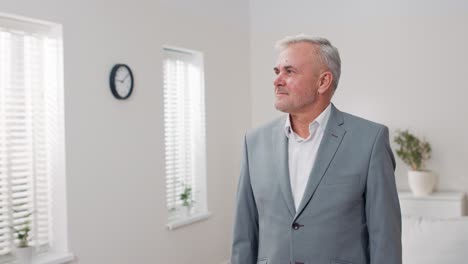 elegant man in grey suit stands against white wall in room, guy has arms crossed on chest smiles at camera real estate agent insurance agent corporate employee office worker businessman