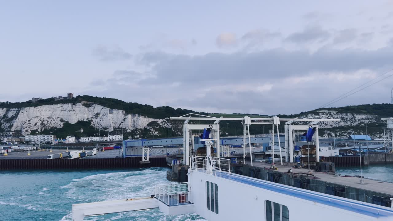 Ferry departs from the port of Dover, England. White cliffs and castle in the distance. Camera pans from left to right