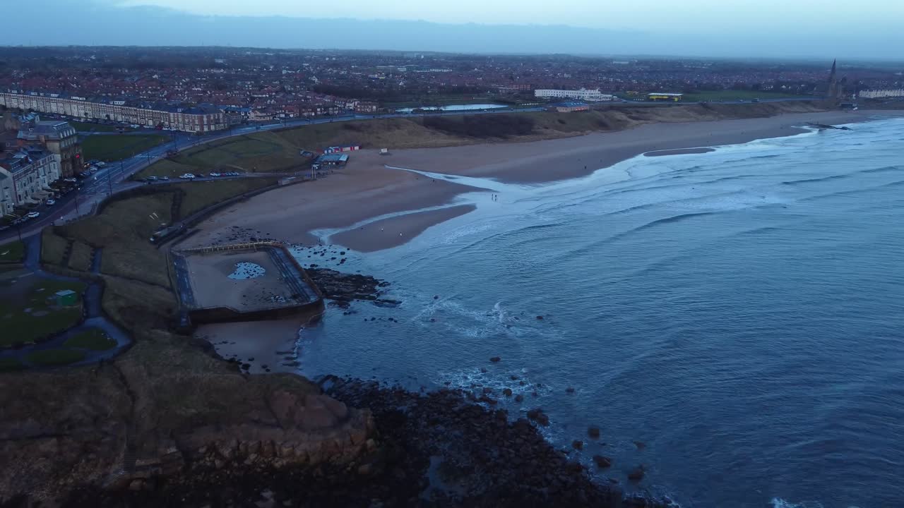 Drone retreating to reveal Tynemouth coast with Longsands beach, outdoor pool and town