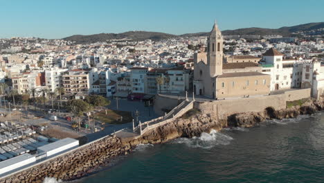 La-Antigua-Iglesia-De-Piedra-Se-Encuentra-En-La-Costa,-Rodeada-De-Casas,-Mientras-Las-Olas-Chocan-Contra-Sus-Paredes