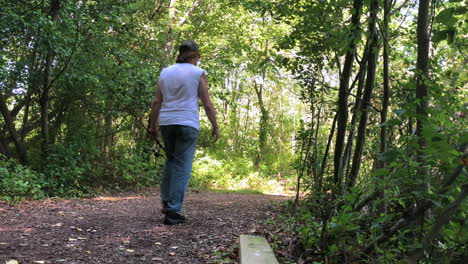 a man walking away from the camera down a path holding a fishing pole