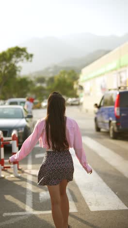 woman crossing the street in a pink shirt and floral skirt