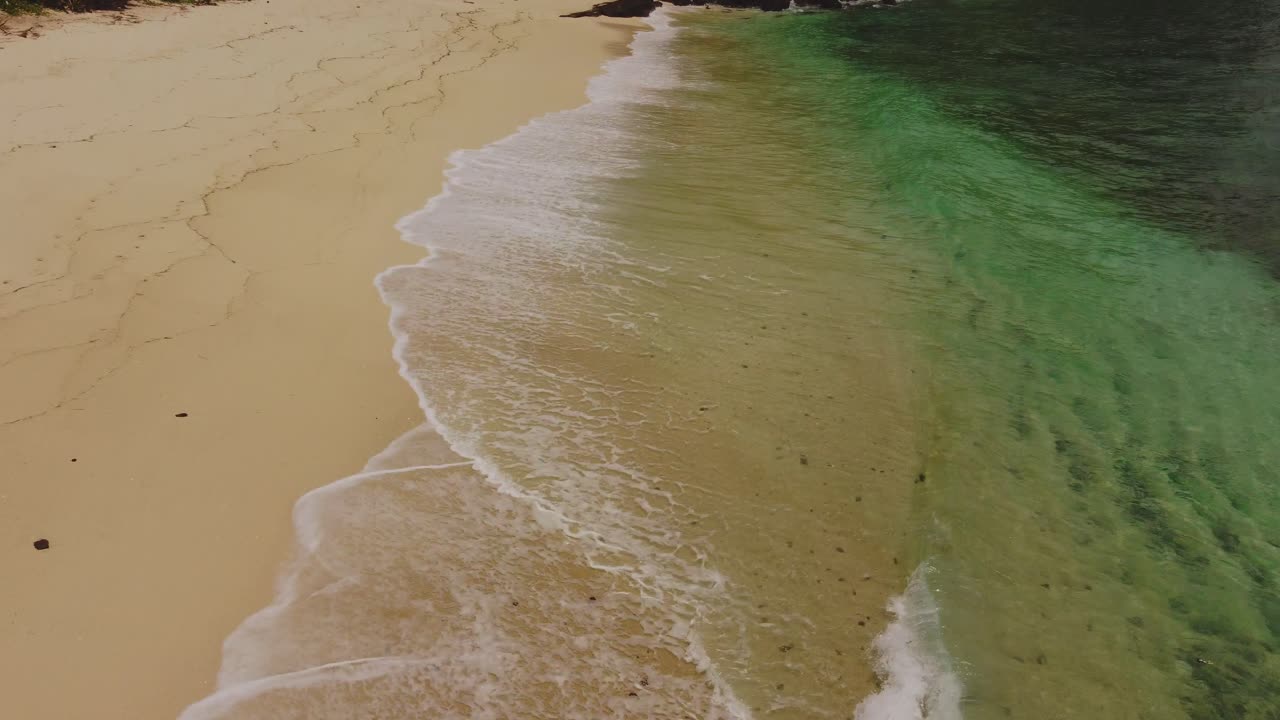 Drone shot of Merese Beach near Kuta Lombok, showing turquoise waves washing over pristine golden sand in tropical scenery.