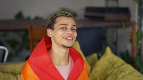 hombre guapo rizado sosteniendo la bandera del arco iris en casa