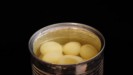 a piece of longan fruit is dropped into an open can of syrup, causing a splash. the scene is brightly lit against a black background with a static overhead camera angle