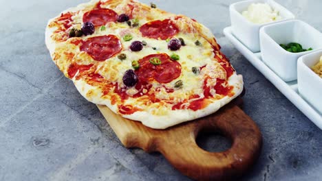 Baked-pizza-with-olive-and-peperoni-toppings-served-on-chopping-board