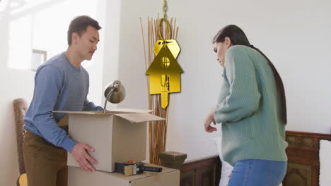 Animación-De-Una-Llave-Dorada-Y-Una-Casa-Sobre-Una-Pareja-Diversa-Llevando-Cajas-De-Cartón-En-Casa