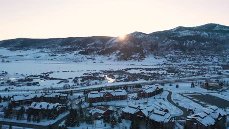 Carretera-En-La-Nieve-Con-Coches-Que-Viajan-Durante-La-Puesta-De-Sol-En-Steamboat-Springs,-Colorado,-EE.UU.