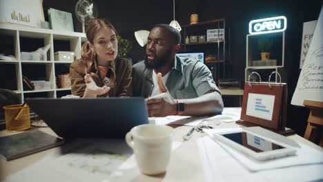 playful afro man and hipster girl talking about data on laptop screen in office.