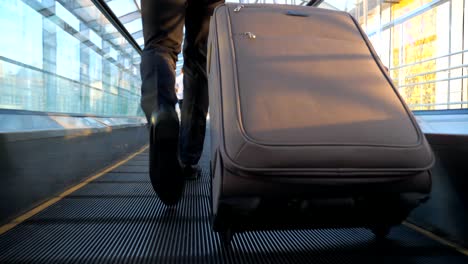 feet of wealthy businessman walking in hall of terminal with his luggage. camera follow to young man with his baggage is being on his way to flight. concept of business trip. back view slow motion