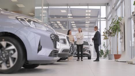 un joven vendedor de coches mostrando a una pareja de jóvenes un nuevo automóvil en el salón de concesionarios.