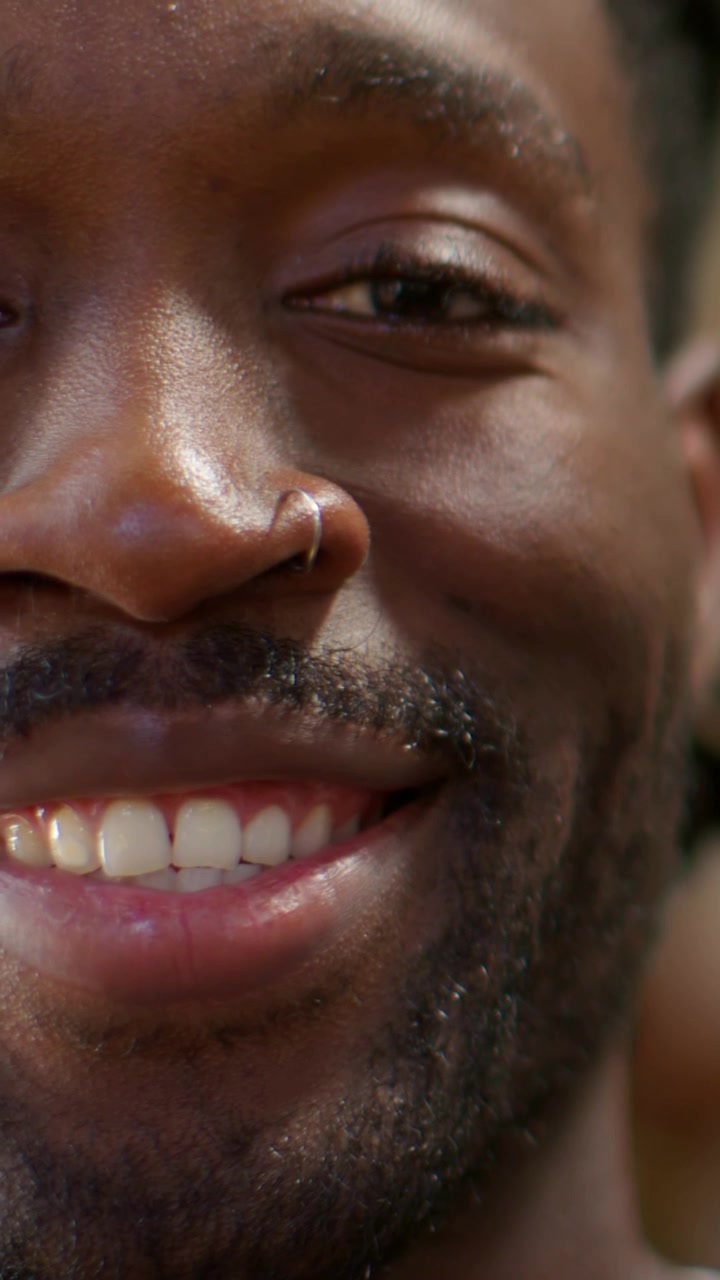 Vertical video: Rolling clip adult male nose-ring beard blinking smiling in warm room with teeth