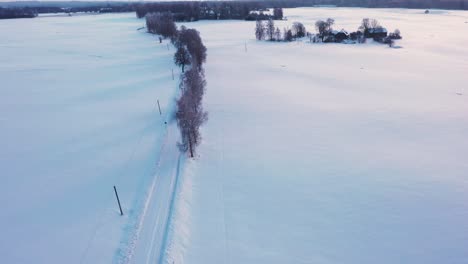 Granjero-Que-Transporta-Fardos-De-Heno-En-Una-Carretera-Helada-De-Invierno-Con-Tractor,-Vista-Aérea-De-Drones