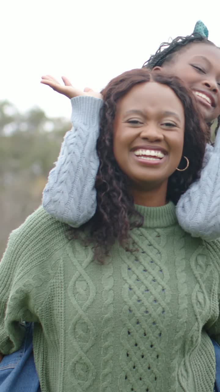 Vertical video: Climbing kid starting playful piggyback woman carrying in park green sweater hoops