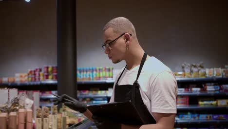 salesman in apron using tablet counting goods in supermarket, regular inventory to control goods, slow motion