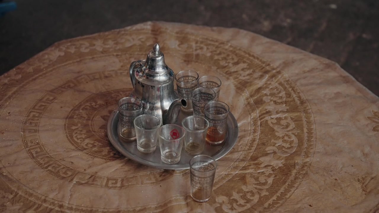 Traditional Moroccan Silver Teapot With Tea Glasses On Metal Tray On Patterned Table