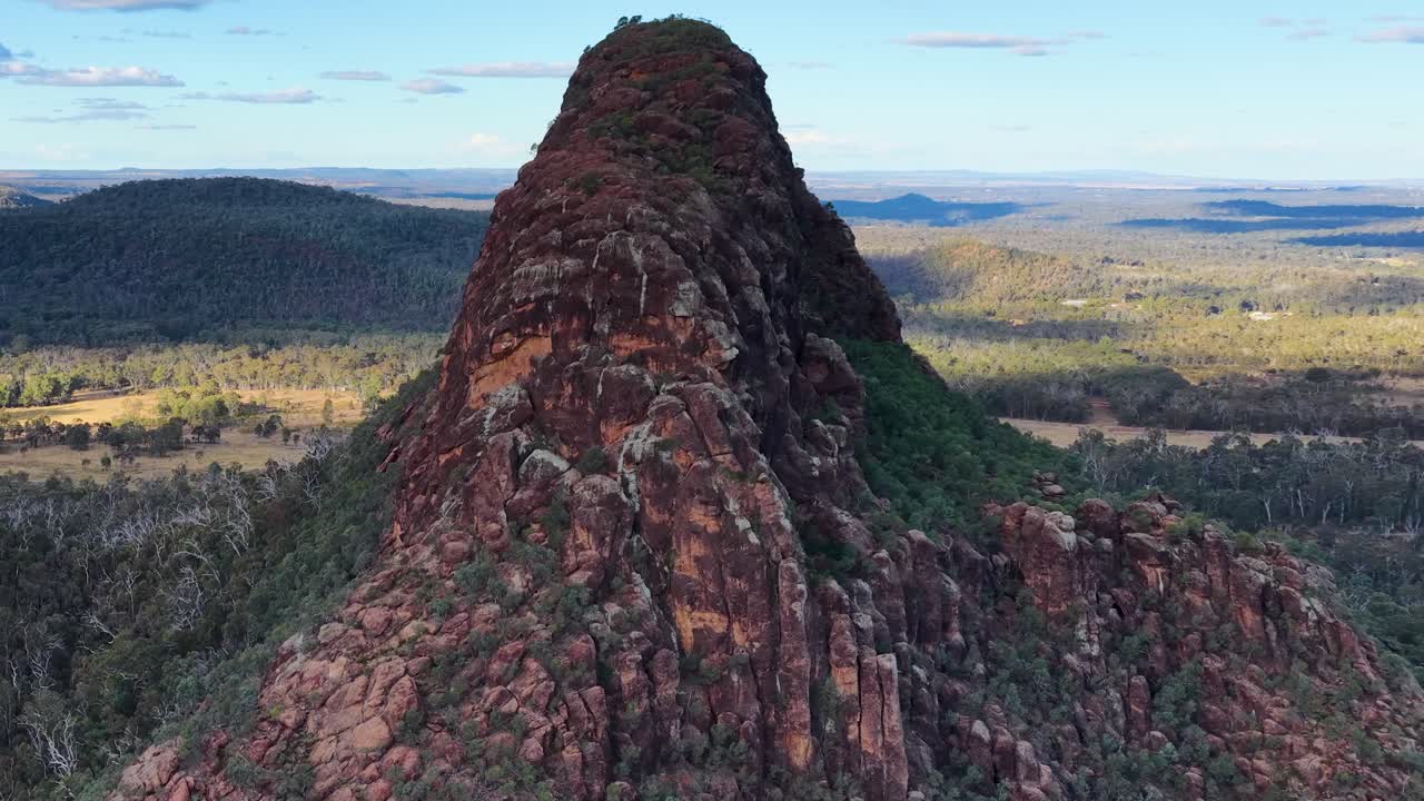 Drone glides toward rugged volcanic outcrop, revealing expansive Australian landscape under soft evening light