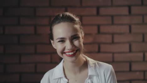 cheerful woman laughing and posing to camera in studio with brick wall