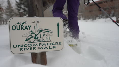 close up, female legs in showshoes walking by ouray uncompahgre river walk sign in snow capped landscape