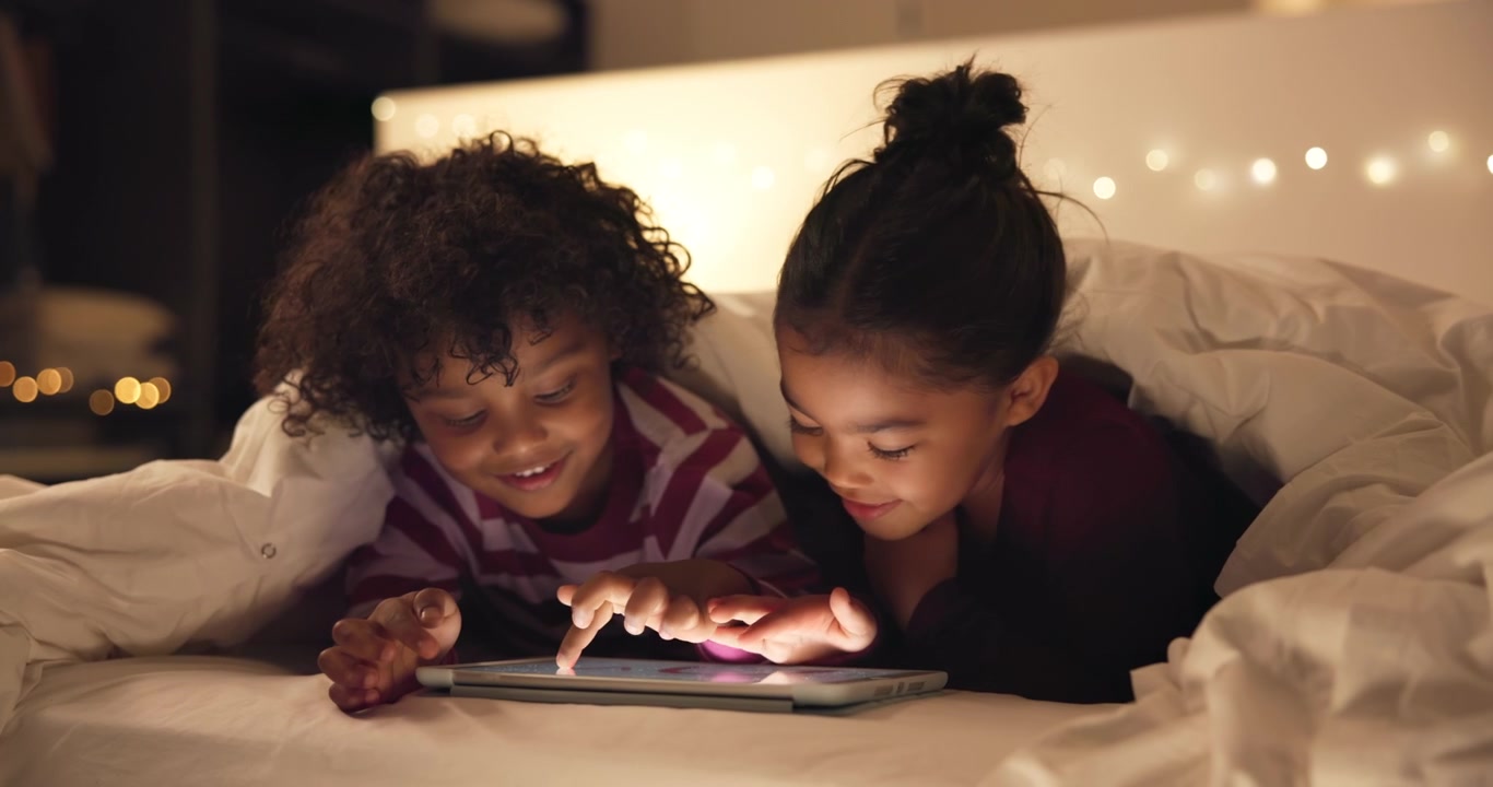 Two Children Using a Tablet Together in Bed at Night