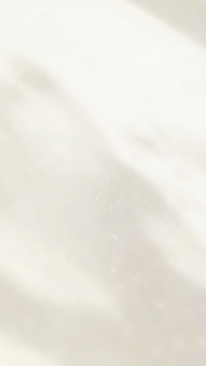 Vertical video: Shifting sunlight revealing specks and diagonal shadows on ivory drape close-up