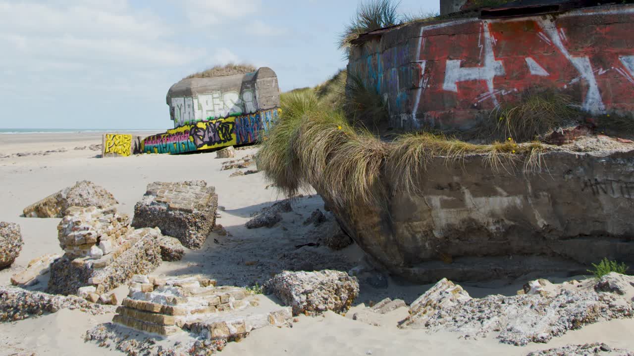 Daytime camera pan reveals historic, graffiti-covered bunkers and sand dunes on Dunkirk coastline
