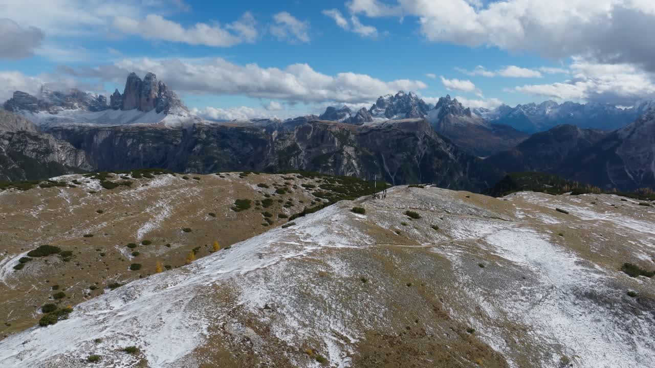 A drone circular view of the top of Platzwiese hike on a partly cloudy day in the Dolomites. The famous Tre Cime is visible from the top of this hike and it's partly snowy already