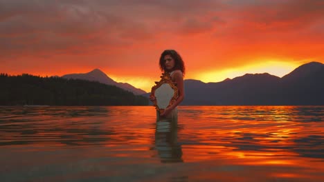 dreamy cinemagraph - seamless video loop of a beautiful young model woman standing in the calm waves of lake walchensee in southern germany-bavaria in a white fashion dress by sunset, facing the sun.