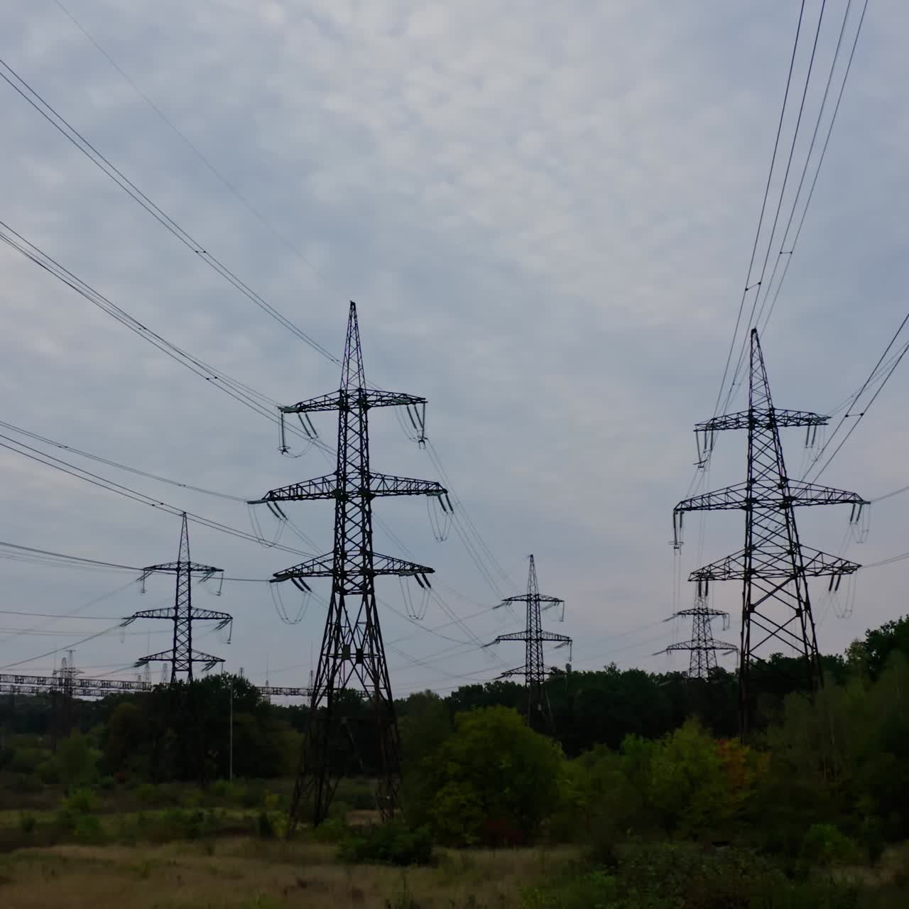 High voltage electricity towers. Power lines at green field in a summer day. Electricity distribution station. View from below.