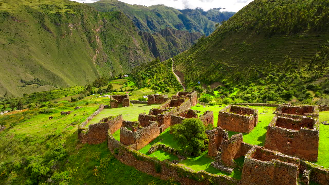 Sito archeologico di Purmamarca, che mostra antiche rovine e terrazzamenti Inca su un fianco di montagna di un verde vibrante in Perù. Drone aereo in volo orbitante.