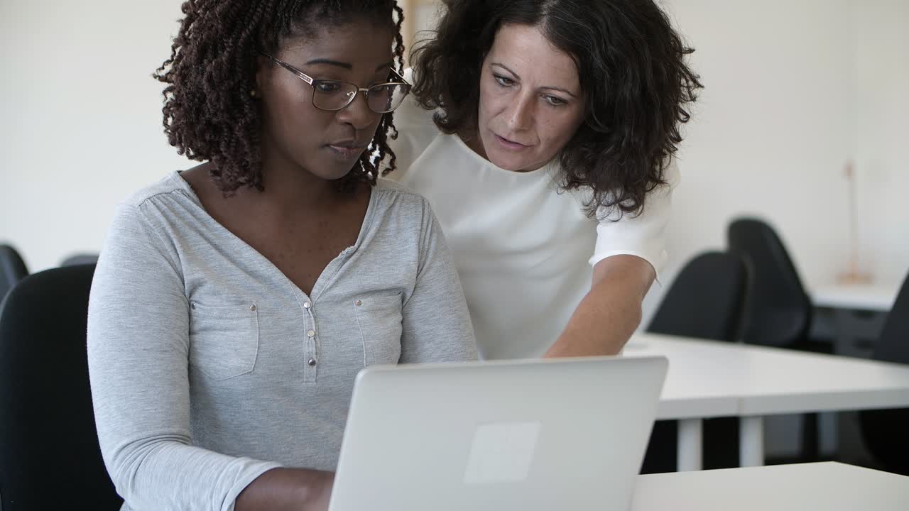 Two focused workers talking and looking at laptop.