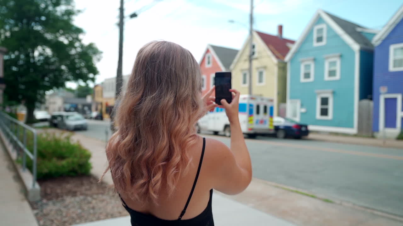 Woman taking photo of colourful buildings on her cell phone in Halifax, Nova Scotia, Canada