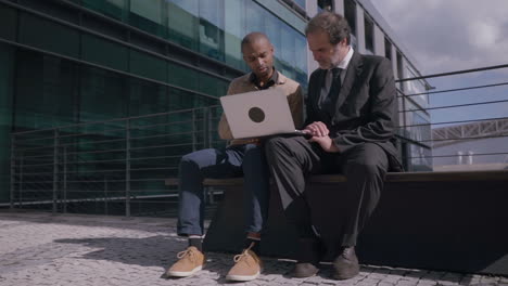 multicultural businessmen with laptop shaking hands on meeting outdoors