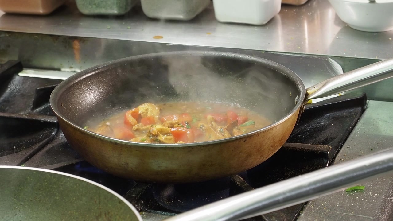 Chicken Tikka Masala sobbolle con pomodoro, verdure e spezie in una padella su fiamma a gas in una cucina indiana professionale, con vapore che sale, primo piano statico