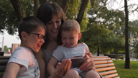mother and two sons laugh while watching mobile phone together in park