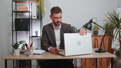 Businessman-freelancer-enters-office-workplace,-working-on-laptop-computer,-sends-online-messages