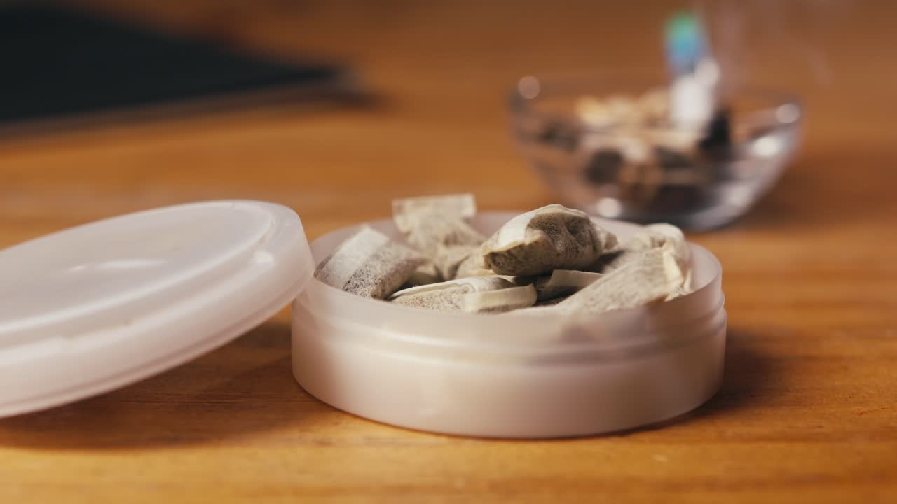 Snus nicotine tobacco close up, pack of tobacco for gum. unhealthy addiction. Man opening box with snus and taking one.